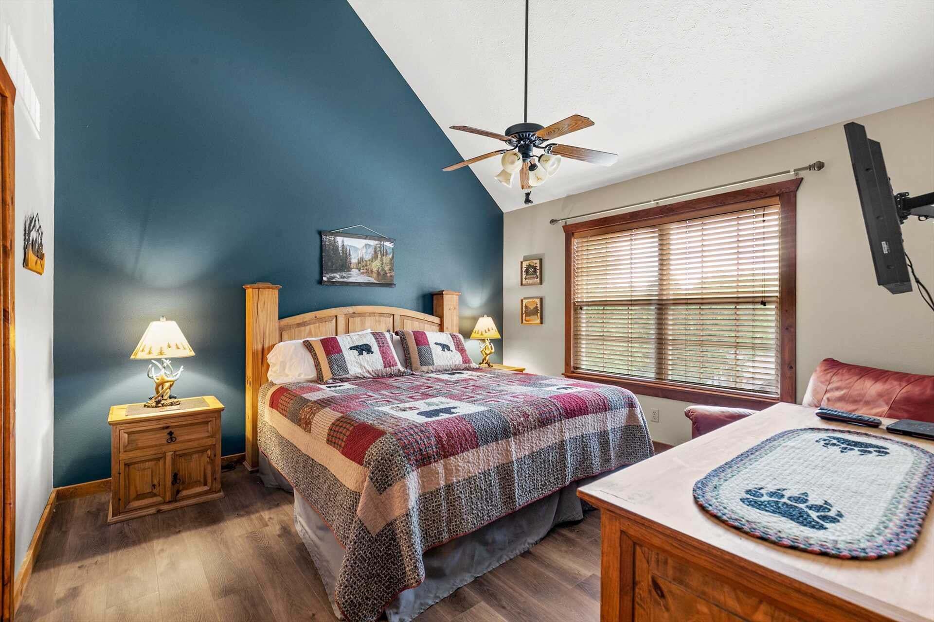 Une chambre à coucher comprenant un lit, une table de chevet en bois, un bureau, une chaise, une fenêtre avec des stores et un ventilateur de plafond.