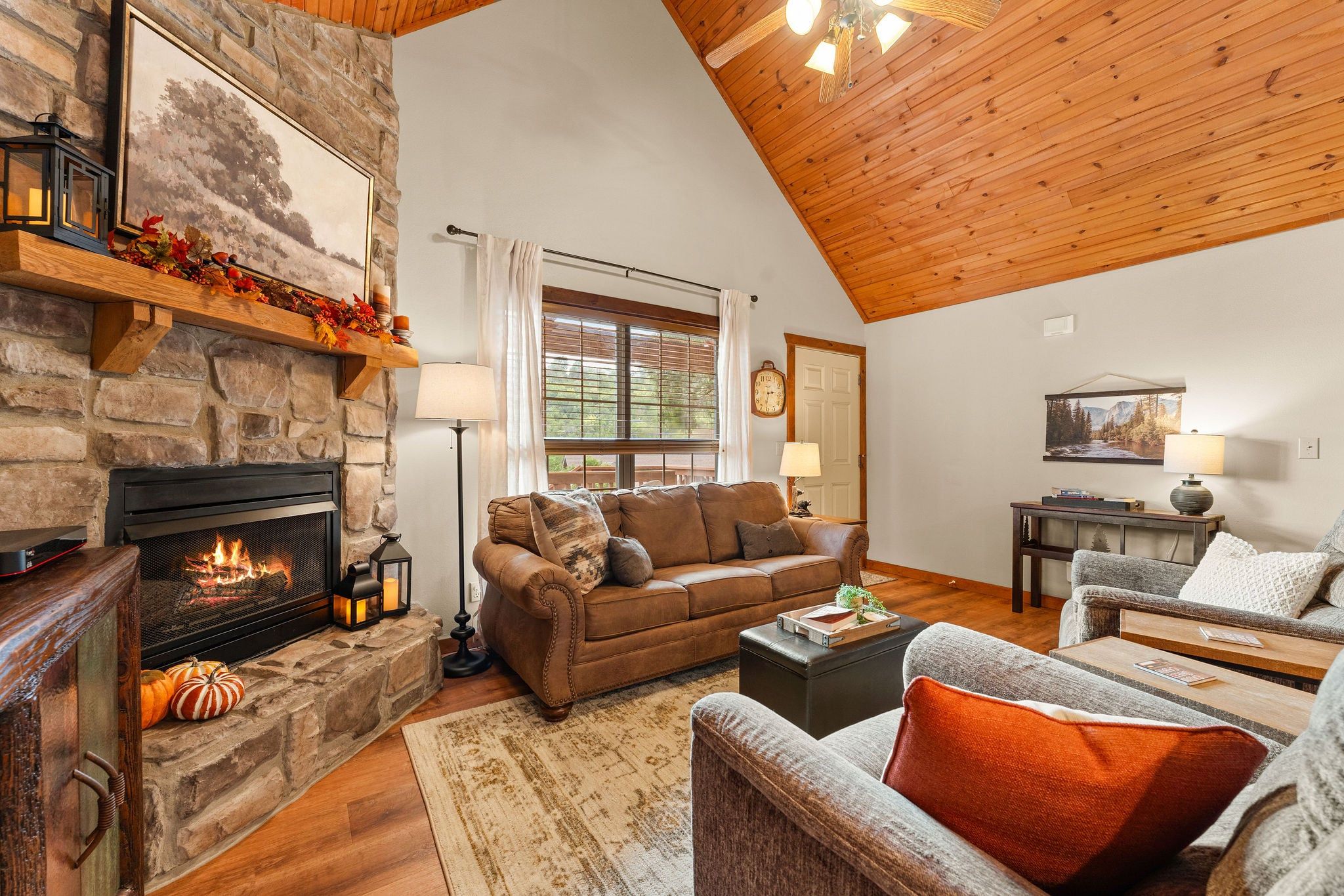 A cozy living room with a stone fireplace, a wooden ceiling, and a large window.