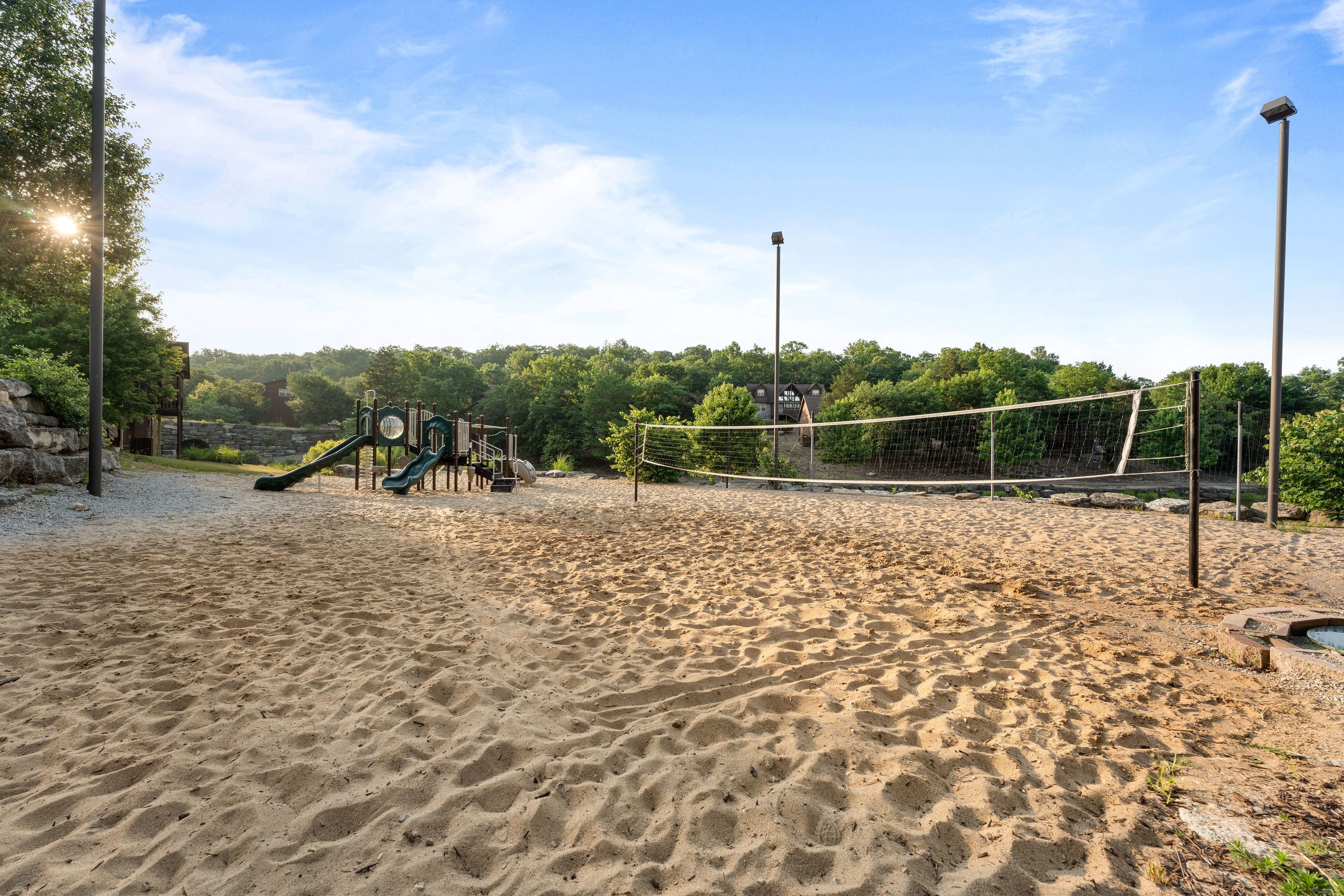 A sandy outdoor area with a volleyball net, a slide, and a playground structure.