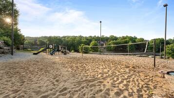 A sandy outdoor area with a volleyball net, a slide, and a playground structure.