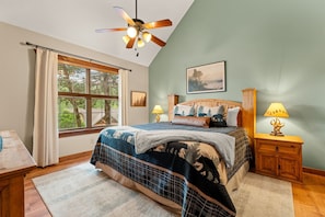 A bedroom with a bed, two bedside tables, a ceiling fan, and a window with curtains.
