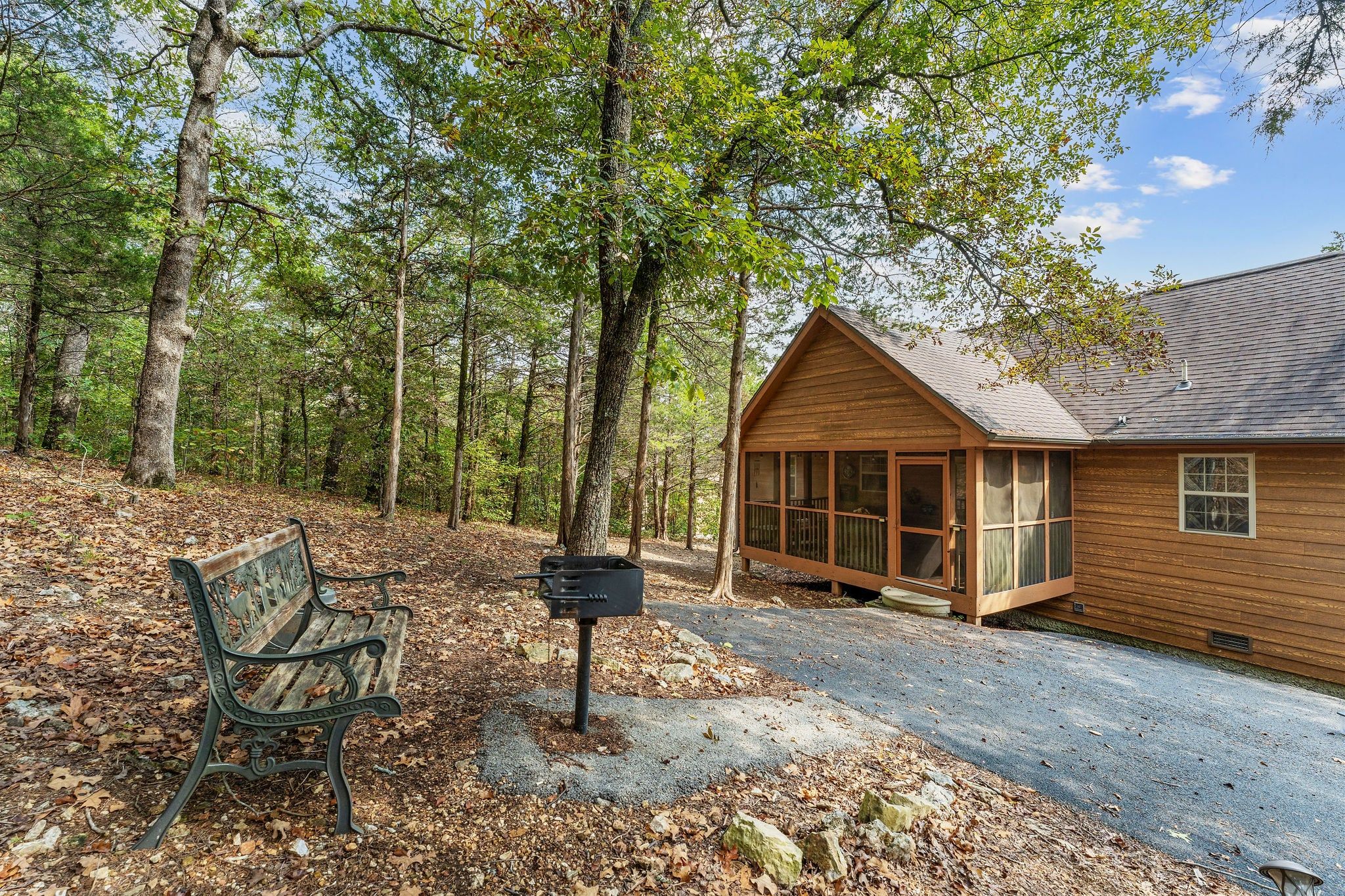 A cabin with a porch, a bench, and a mailbox in a wooded area.