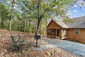 A cabin with a porch, a bench, and a mailbox in a wooded area.
