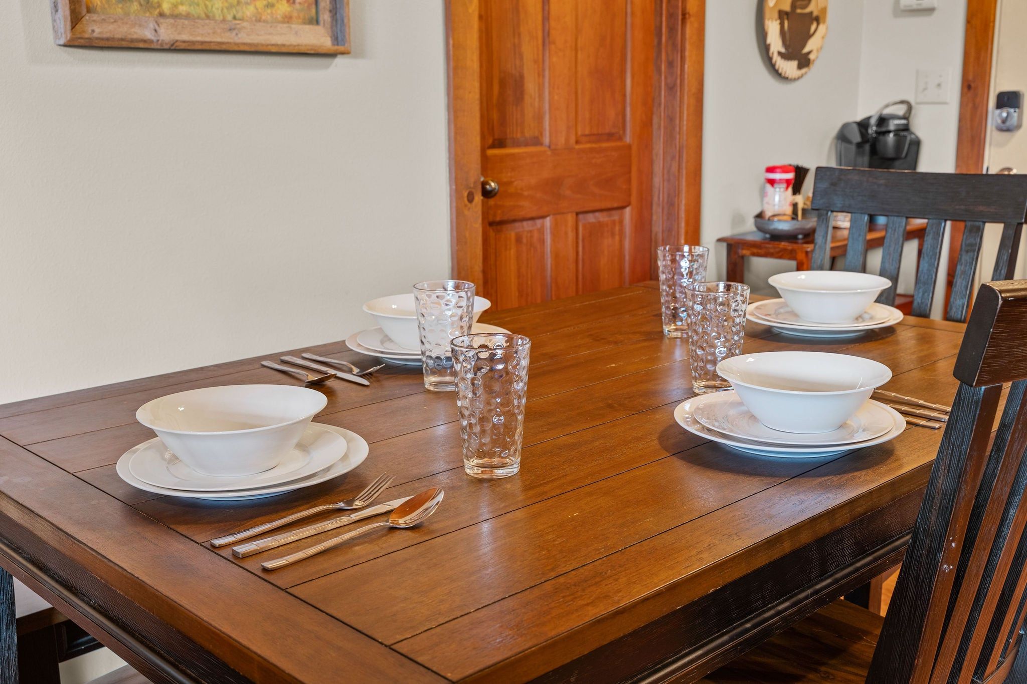 A wooden dining table set for four with white dinnerware and clear glassware.