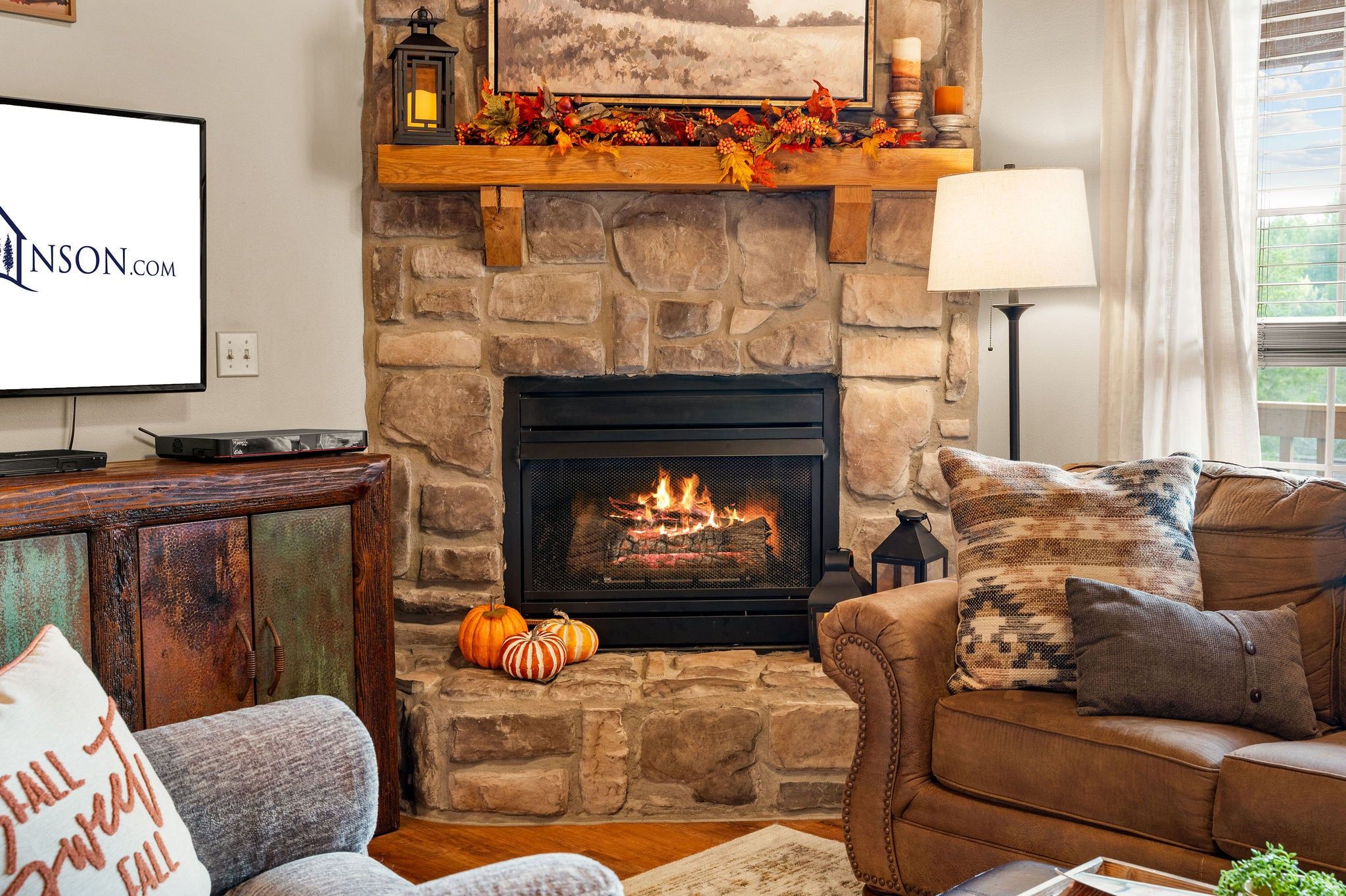 A cozy living room with a stone fireplace, a television, and a comfortable couch.