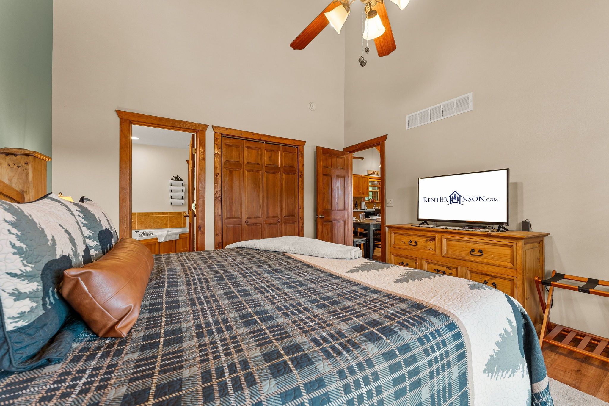 A bedroom with a bed, a wooden dresser, a television, and a ceiling fan.
