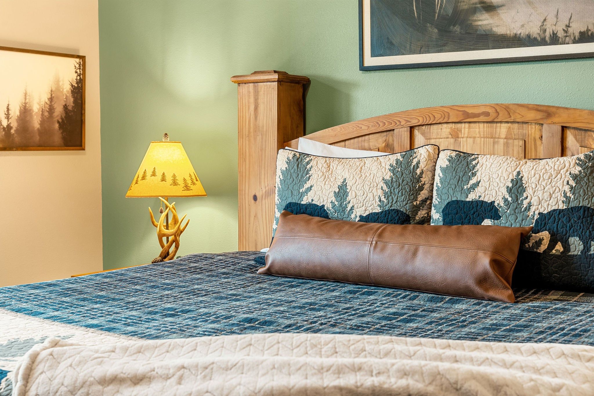 A bed with a quilted headboard, a brown leather pillow, and a patterned pillow.