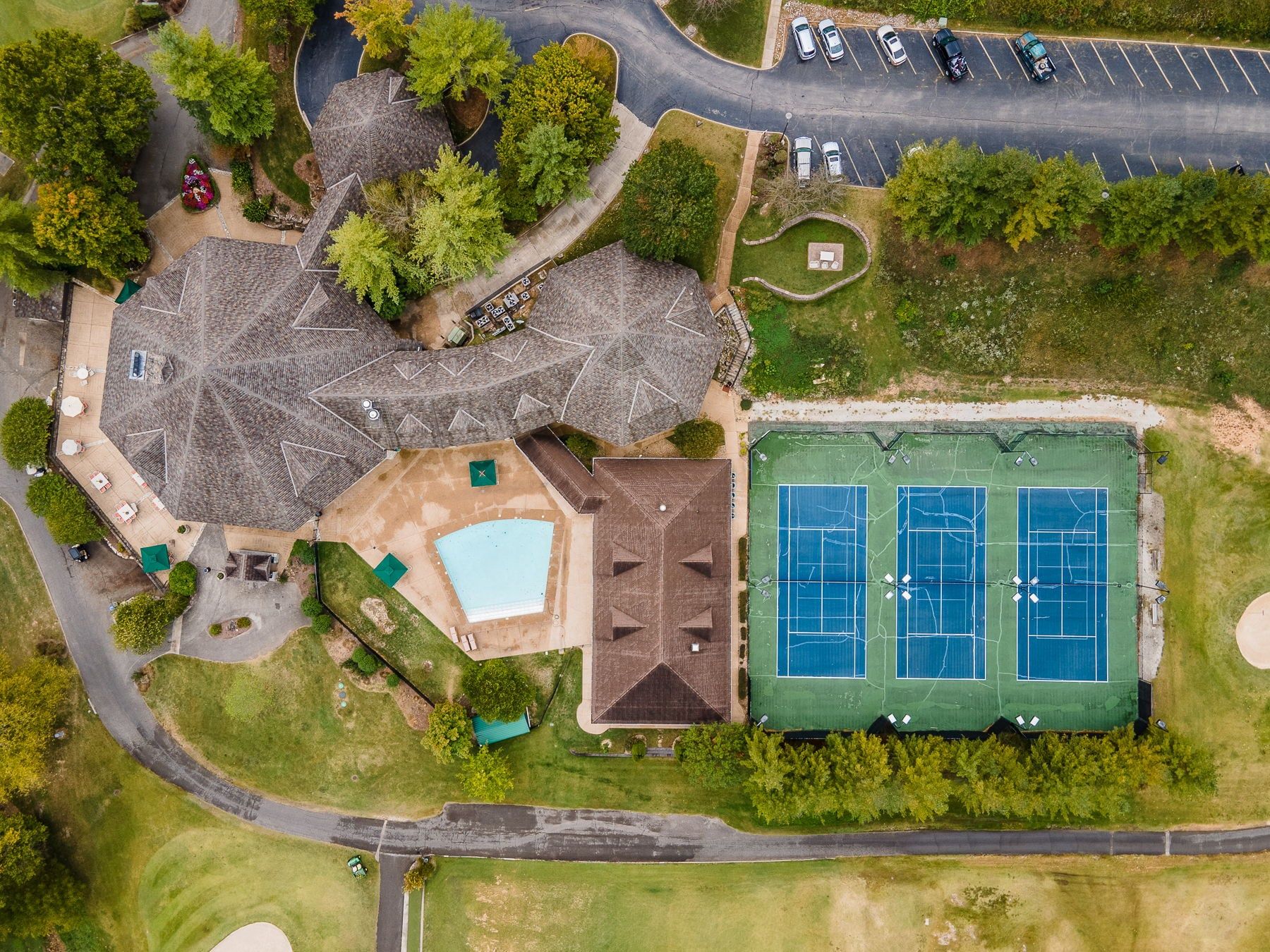 An aerial view of a property with a tennis court, a swimming pool, and a parking lot.