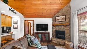 Un salon chaleureux avec une cheminée en pierre, un téléviseur et un plafond en bois.