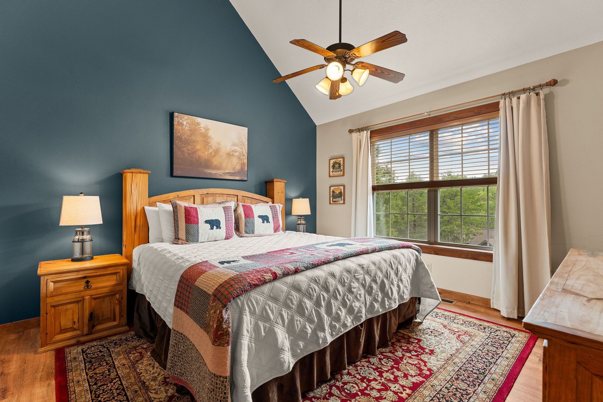A bedroom with a bed, a nightstand, a lamp, a ceiling fan, a window with curtains, and a rug.