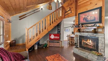 Un vaste salon doté d’un escalier en bois, d’une cheminée et d’un téléviseur fixé au mur.