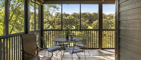 Un espacio al aire libre techado con una mesa, sillas y un banco, con vista a un área boscosa.