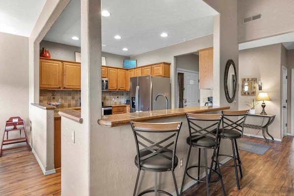A kitchen with wooden cabinets, stainless steel appliances, and a bar area with stools. - Beautiful Golf Course view, Near SDC, Lots of Space, Free Daily Attraction Tickets (Branson West)