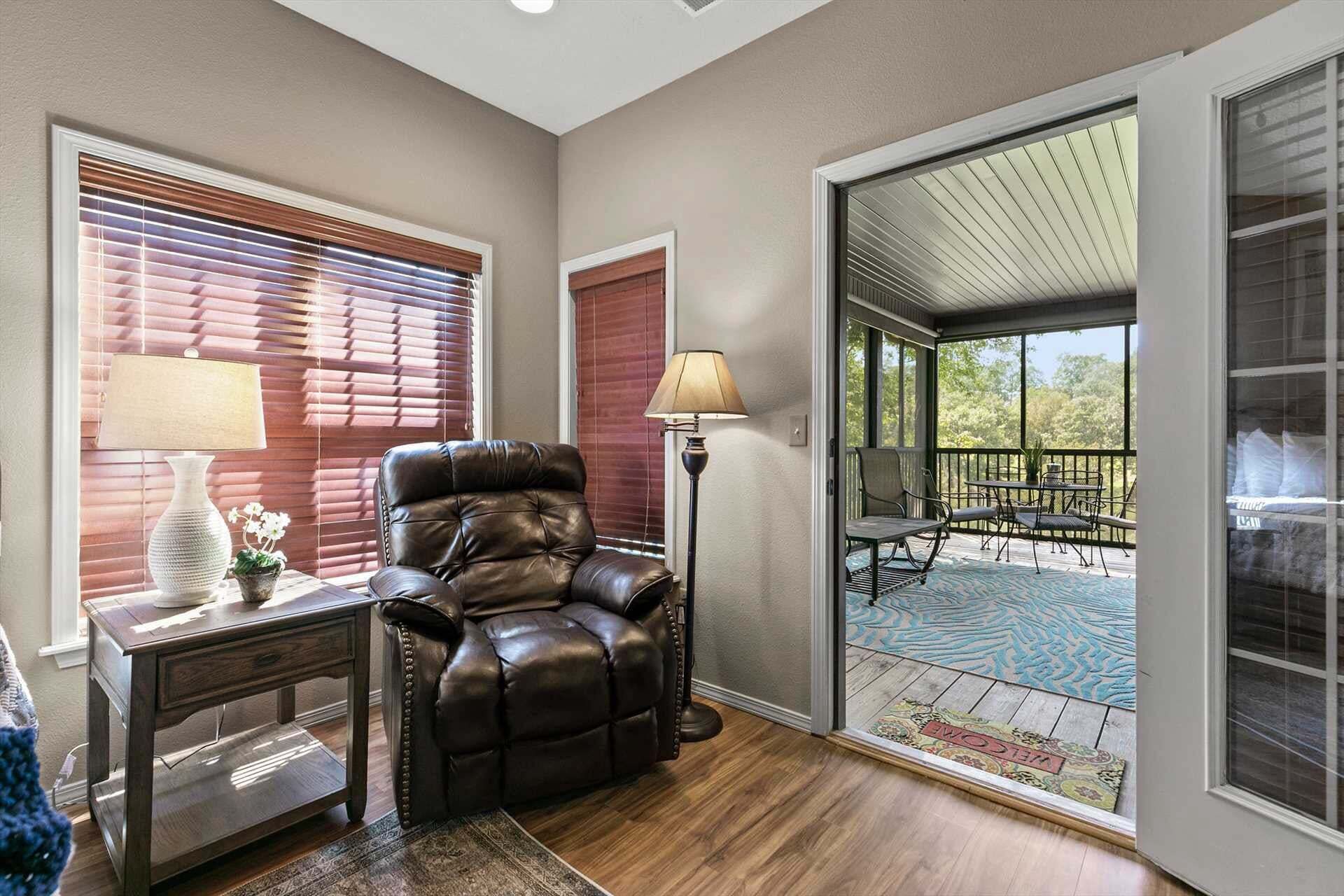 A room with a leather recliner, a desk with a lamp, and a view of an outdoor patio with furniture.