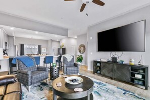 Ein modernes Wohnzimmer mit Flachbildfernseher, einer Couch, einem Couchtisch und einem Essbereich im Hintergrund.