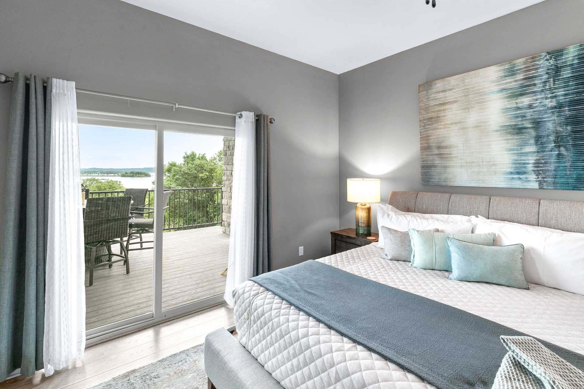 Une chambre dotée d’un grand lit, d’une table de chevet, d’une lampe et offrant une vue sur un espace extérieur aménagé avec une chaise et une table, accessible par une porte-fenêtre coulissante.