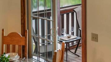 A dining area with a table set for two, a wooden chair, and a view through a glass door to an outdoor deck.
