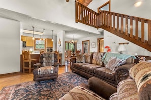 A spacious living room with a large brown leather sofa, a patterned armchair, and a wooden staircase. - Stonebridge Lodge, Water Views, Gated Community, Free Daily Attraction Tickets (Branson West)