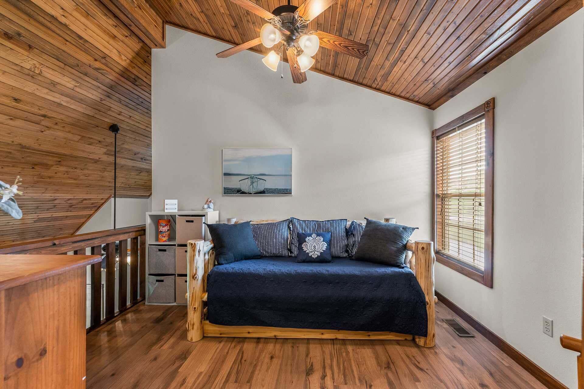 A room with a wooden ceiling, a ceiling fan, a sofa with patterned cushions, a painting on the wall, and a window with blinds.