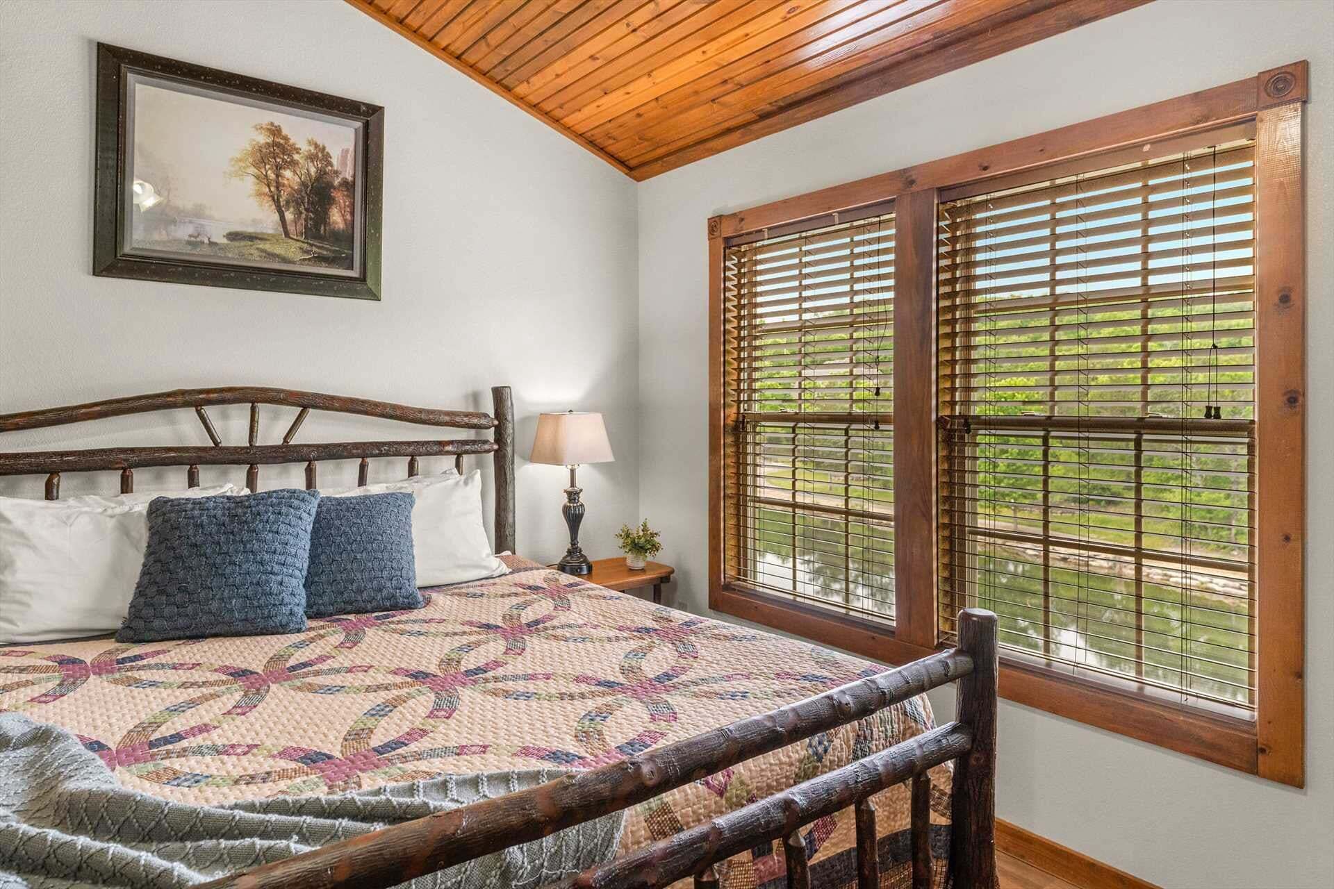 A bedroom with a wooden headboard, a quilt, a bedside lamp, and a window with blinds.