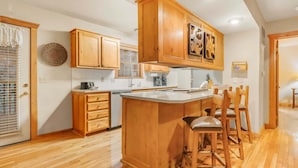 A kitchen with wooden cabinets, a central island with bar stools, and a window with blinds. - Private lodge near Silver Dollar City, Beautiful Pool,. Fishing Lake, Ramp Entry, Vaulted Ceilings (Branson West)