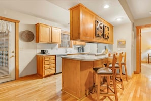 A kitchen with wooden cabinets, a central island with bar stools, and a window with blinds. - Private lodge near Silver Dollar City, Beautiful Pool,. Fishing Lake, Ramp Entry, Vaulted Ceilings (Branson West)