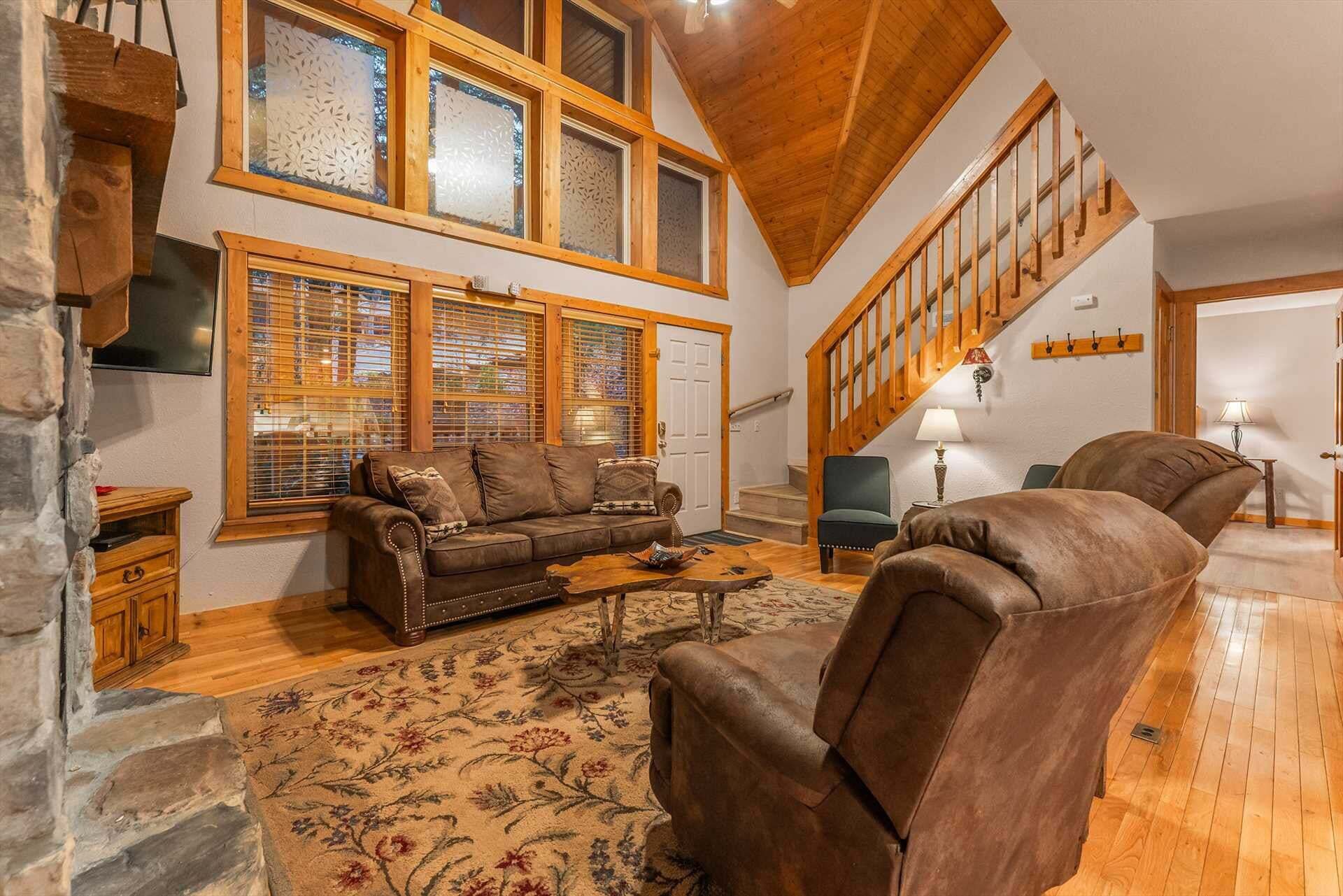 A spacious living room with a high ceiling, a wooden staircase, and a stone wall.