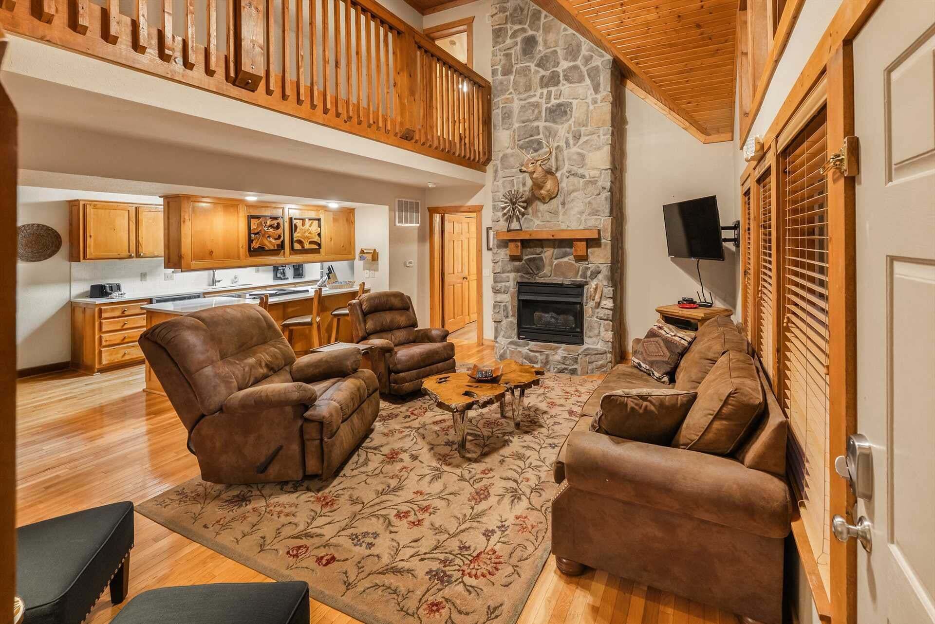 A spacious living area with leather sofas, a stone fireplace, and a kitchen in the background.