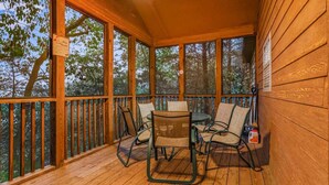 A wooden deck with a table and chairs, surrounded by glass windows. - Private lodge near Silver Dollar City, Beautiful Pool,. Fishing Lake, Ramp Entry, Vaulted Ceilings (Branson West)