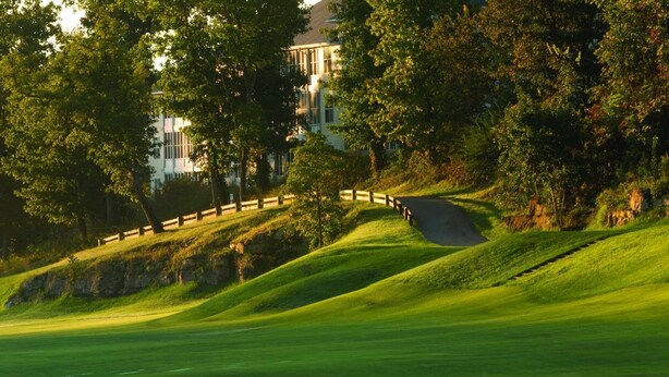 A golf course with a wooden fence, rolling green hills, and a building in the background. - Private lodge near Silver Dollar City, Beautiful Pool,. Fishing Lake, Ramp Entry, Vaulted Ceilings (Branson West)