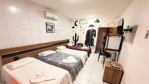 A hotel room with three beds, a TV, a desk, and a wall with a cactus and cowboy-themed artwork. - Pousada Oásis do Cariri (Juazeiro do Norte)