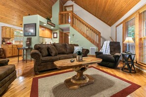 A spacious living room with a wooden ceiling, a brown leather sofa, a wooden coffee table, and a staircase leading to an upper level. - Near SDC, Private Lake and Fishing, Free Daily Attraction Tickets (Branson West)