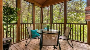 A wooden deck with a table and chairs, surrounded by glass panels and a view of trees. - Private Lodges near Silver Dollar City, Private Lake and Fishing, Beautiful Pool (Branson West)