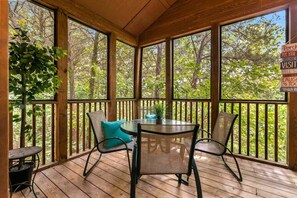 A wooden deck with a table and chairs, surrounded by glass panels and a view of trees. - Private Lodges near Silver Dollar City, Private Lake and Fishing, Beautiful Pool (Branson West)
