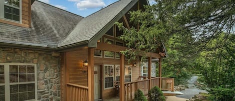 A two-story stone house with a wooden porch, stone walls, and a stone staircase leading to the entrance.