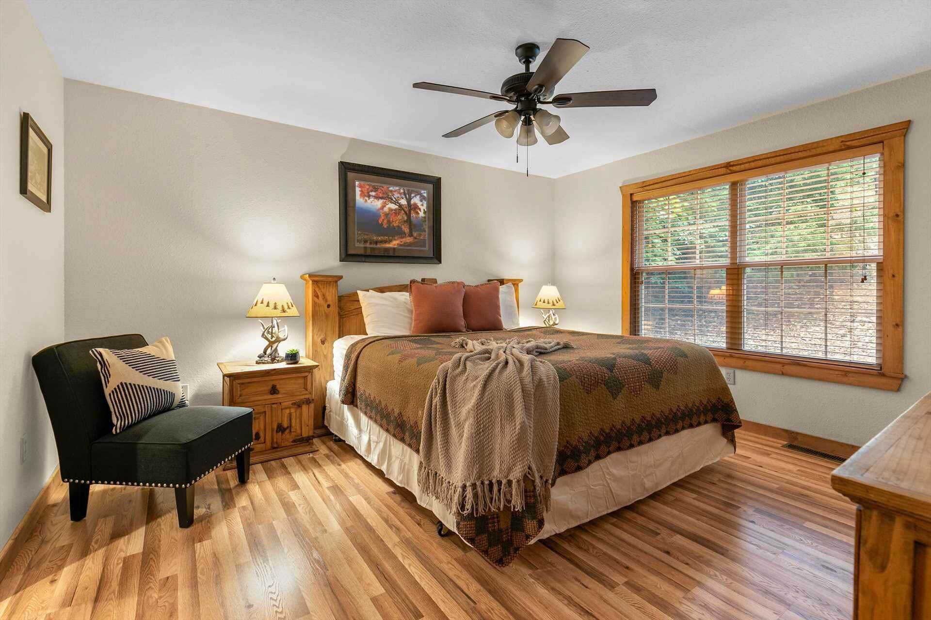 Une chambre à coucher comprenant un lit, une chaise, une table de chevet, une lampe, un ventilateur de plafond et une fenêtre.