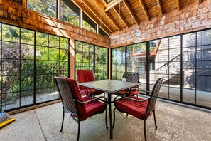 Une terrasse couverte avec une table et des chaises, de grandes fenêtres et une vue sur la verdure.