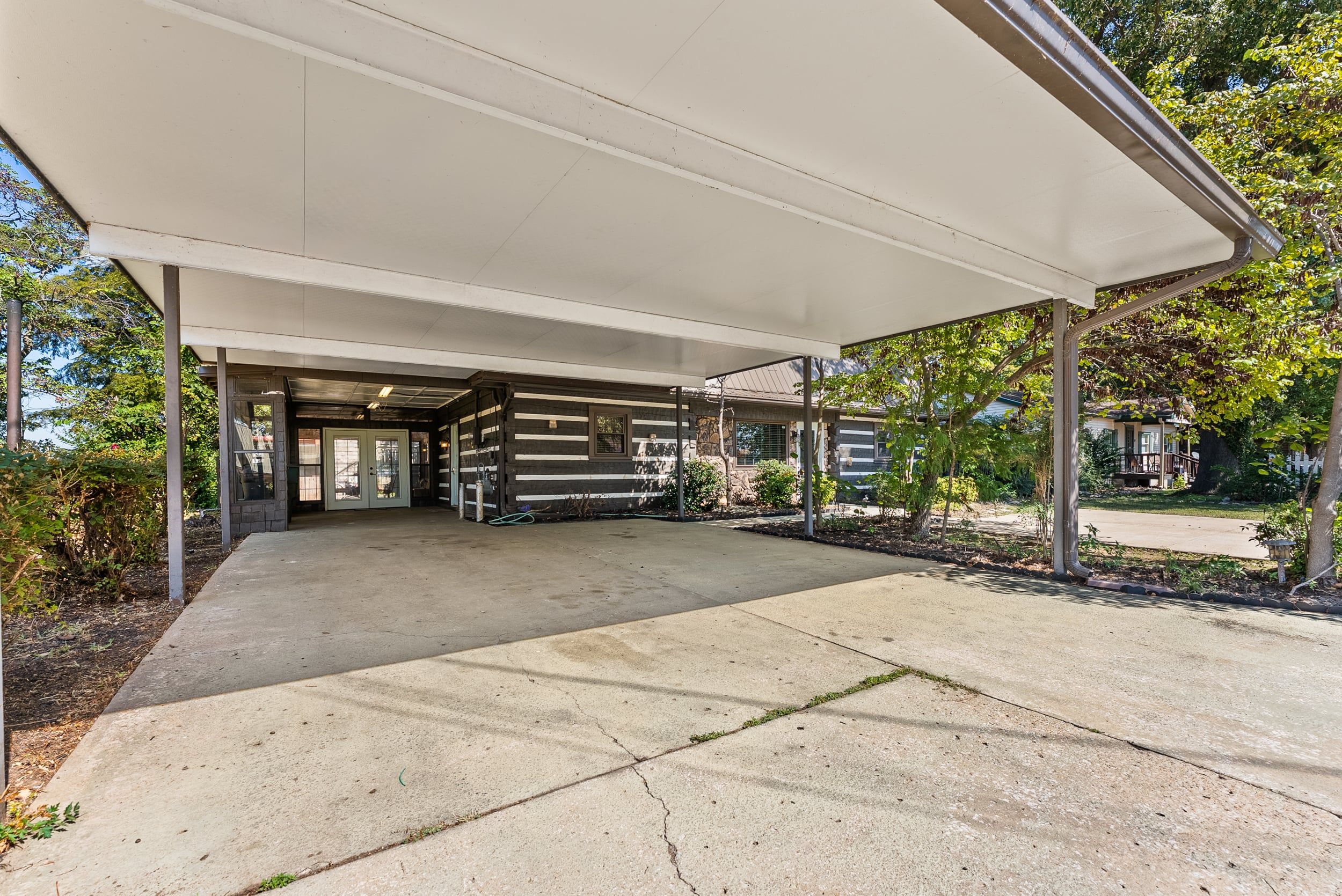 A covered outdoor area with a concrete floor, a wooden structure with horizontal siding, and a white canopy overhead.