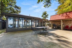 A covered patio area with a table and chairs, a grill, and a view of the water.