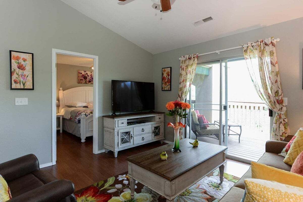 Un salon avec une télévision, une table basse et un canapé. Il y a un balcon avec une chaise et une table.