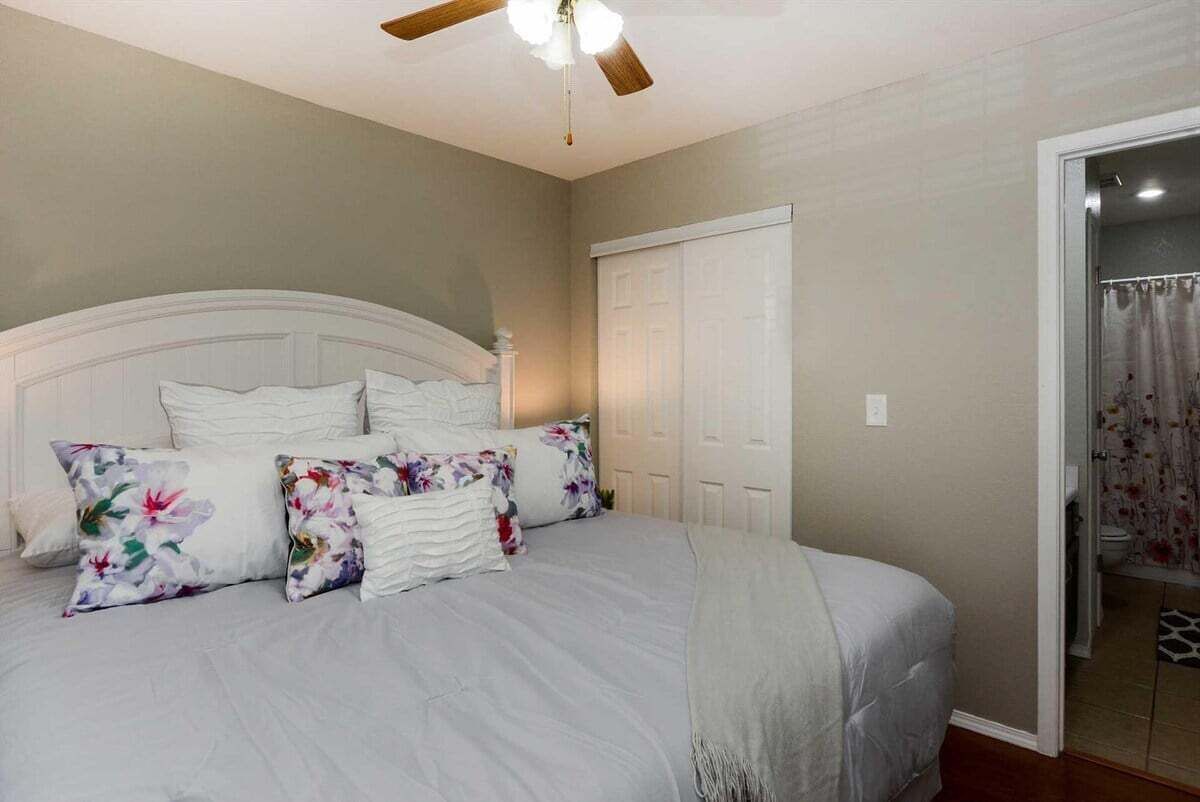 A bedroom with a bed, a ceiling fan, and a door leading to a bathroom.