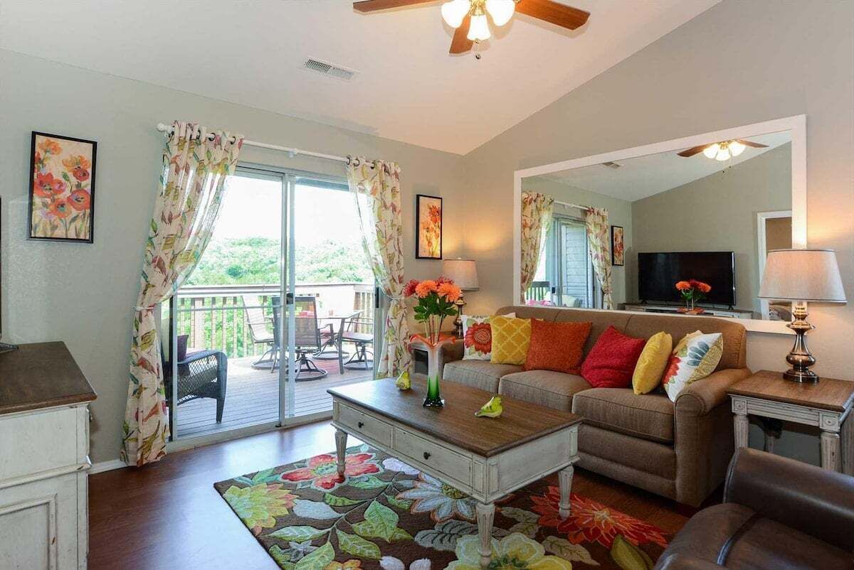 A living room with a sofa, coffee table, and a television. There is a sliding glass door leading to an outdoor patio.