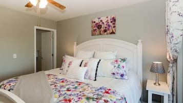 A bedroom with a bed, a ceiling fan, a nightstand with a lamp, and a door leading to another room.