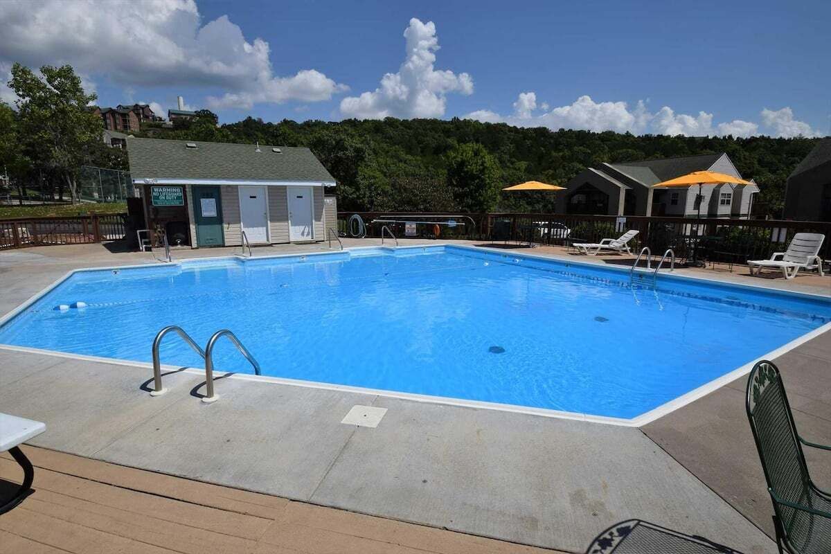 A rectangular swimming pool with a clear blue water surface, surrounded by a deck area with lounge chairs and umbrellas.