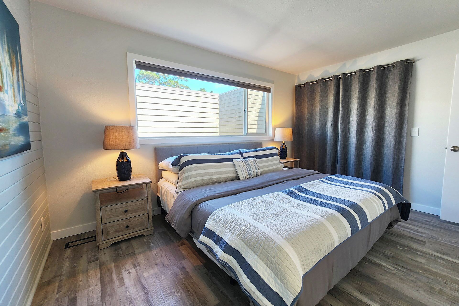 Un dormitorio con una cama grande, dos mesitas de noche, una ventana con persianas y una puerta con cortinas.