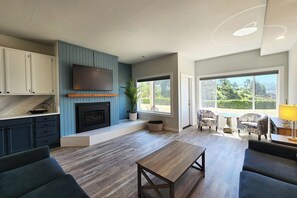 Ein modernes Wohnzimmer mit Kamin, Einbauschränken, einem Flachbildfernseher und einem großen Fenster mit Blick ins Freie.