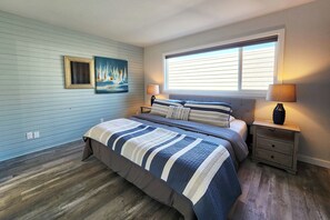 Ein Schlafzimmer mit einem großen Bett, zwei Nachttischen, einem Fenster mit Jalousien, einem Bild an der Wand und einem Holzboden.