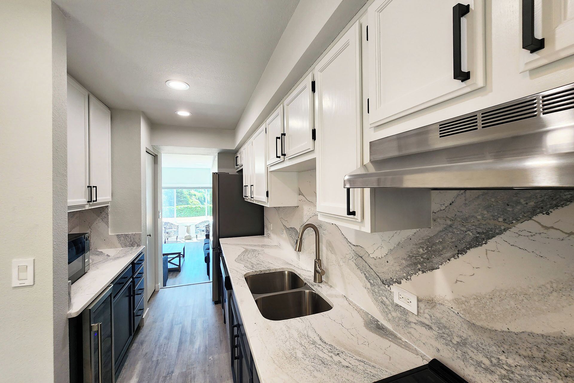 A kitchen with white cabinets, a stainless steel sink, and a marble countertop.