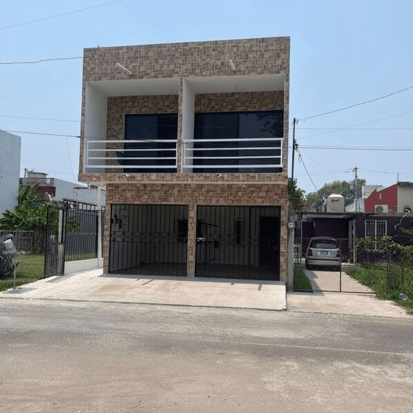 A two-story building with a balcony on the upper floor, a gated entrance, and a parked car in the background.