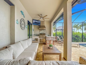 A spacious living area with a sofa, a dining table, and a kitchen area with a TV. - 5 Bedroom, Saltwater Heated Pool & Spa, Dock: The Coastal Cabana (Cape Coral)